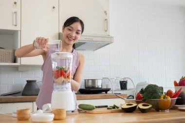 Modern bir mutfakta sağlıklı meyve ve sebzelerle meyve suyu yapan genç bir kadın sağlıklı bir yaşam tarzını destekliyor..