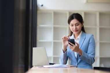 Modern bir ofiste çalışan genç bir muhasebeci, akıllı telefon ve dizüstü bilgisayar kullanarak, mali görevler ve iletişim üzerine odaklanmıştır..