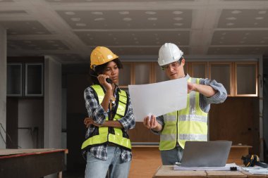 Mühendislik ekibi modern bir şantiyede inşaat planlarını planlar ve güvenlik teçhizatlarıyla tartışıyor..