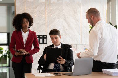 Aralarında bir kadın ve iki erkeğin de bulunduğu üç kişilik çeşitli iş ekibi, bir ofis masasında dizüstü bilgisayarlı, parlak modern ofis ayarlarıyla mali raporları inceliyor.