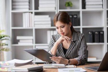 Genç bir kadın iş yerinde stresli, elinde bir tablet, endişeli ve modern bir ofis ortamında bunalmış görünüyor..