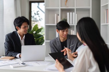 İş dünyasından profesyonellerden oluşan bir ekip, dizüstü bilgisayarlar ve tabletler kullanarak fikir alışverişinde bulunmak ve fikir alışverişinde bulunmak üzere modern bir konferans odasında toplanıyor..