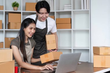 A young couple working together to manage online orders and pack products in their home office, surrounded by cardboard boxes and a laptop. clipart