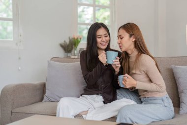 Lezbiyen ve LGBT çifti sıcak bir anı paylaşırken aynı anda rahat ve modern bir oturma odasında kahve içiyorlar..