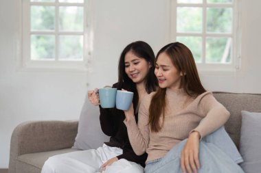 Sevgi dolu lezbiyen bir çift, sıcak ve modern bir oturma odasında kahvelerini yudumluyor, bağlarını ve mutluluklarını sergiliyorlar..