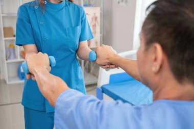 Genç bir bakıcı, modern bir sağlık merkezinde fizyoterapi uygulayan yaşlı bir hastaya şefkat ve profesyonel bakım göstererek yardımcı olur..