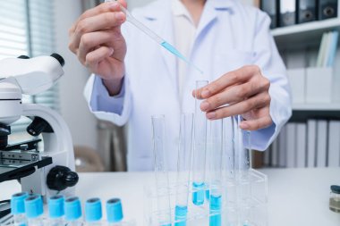 Laboratuvar önlüğü giymiş genç bir araştırmacı modern bir laboratuvar ortamında test tüpleri ve pipetleri kullanarak ilaç araştırmaları üzerinde çalışıyor..