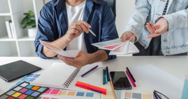 Grafik tasarımcısı, modern bir çalışma alanında yaratıcı tasarım projelerine odaklanarak, bir bilgisayarda renk çiftleri seçiyor.