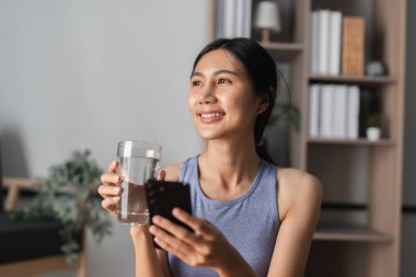 Yogadan sonra huzurlu bir şekilde oturan genç bir kadın, elinde canlandırıcı bir içecek, modern bir ev ortamında rahatlık ve farkındalığı somutlaştırıyor..