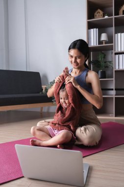 Bir anne ve çocuğu evlerinde yoga seanslarının keyfini çıkarırlar, rahat bir oturma odasında pembe bir paspasın üzerinde oturup egzersiz yaparlar..