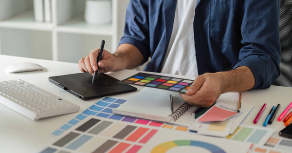 Графический дизайнер, работающий на компьютере, выбирающий цветовые пары для творческих проектов с использованием цифровых инструментов и цветных образцов в современном рабочем пространстве.