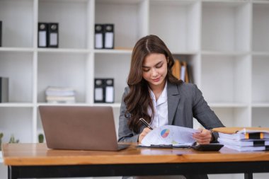 Profesyonel iş kadını işine odaklanmış. Ofis masasında dizüstü bilgisayarla belgeleri analiz ediyor..
