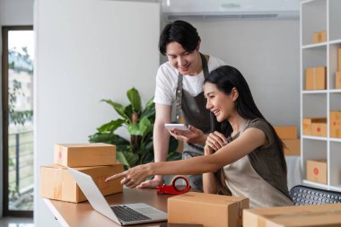 A couple working together in a home office, managing their online business by checking product stock and orders on a laptop. clipart