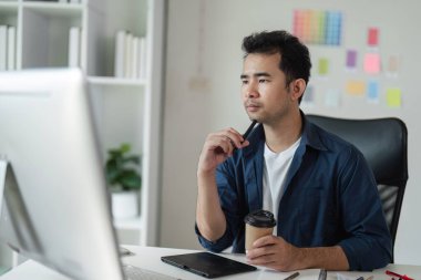 Düşüncelere dalmış bir grafik tasarımcısı, dijital araçlar ve renk örnekleriyle modern ofis ortamında yaratıcı bir proje planlıyor..