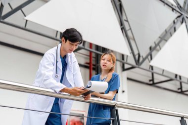 Bir erkek doktor ve danışman asistanı, sağlık hizmetlerindeki takım çalışmalarını vurgulayarak çağdaş bir binanın dışında konuşmaya girişirler..