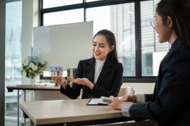 Modern bir ofisteki bir işadamı ev satın almak için sözleşme imzalıyor, gayrimenkul işlemlerini ve profesyonel iş anlaşmalarını sembolize ediyor.