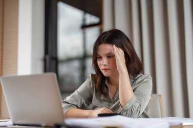 Çalışma materyalleriyle çevrili, modern bir ofis ortamında masasında stres yaşayan bir iş kadını..