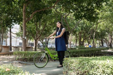 A young woman enjoys riding her bike in a park embracing clean energy and reducing pollution. clipart