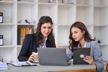 İki iş kadını, modern ofis ortamında teknolojiyi kullanarak iş arkadaşlarıyla ortak bir tartışmaya giriştiler..