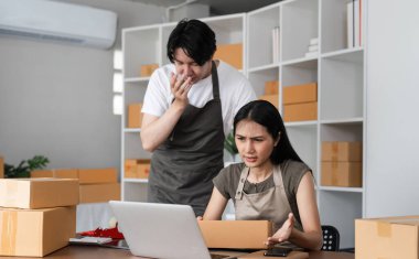 Paketlerle çevrili ve dizüstü bilgisayar kullanarak evlerinden online iş siparişlerini yönetirken stresli ve ciddi hisseden bir çift..