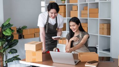 Bir çift ev ofislerinde işbirliği yapıyor, kutu paketliyor ve çevrimiçi satışları yönetiyor, takım çalışması ve girişimcilik sergiliyor.