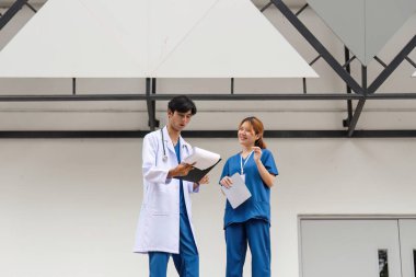 Bir erkek doktor ve danışman asistanı, profesyonel etkileşim ve takım çalışması sergileyerek çağdaş bir binanın dışında çalışmayı tartışır..