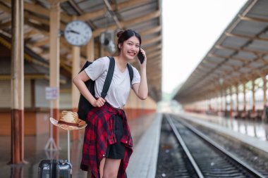 Tatlı genç bir kadın tren istasyonunda duruyor, gülümsüyor ve telefonda konuşuyor, seyahat macerasına hazır..