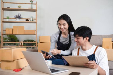 Ofislerinde birlikte çalışan genç bir çift e-ticaret işleri için online siparişler alıyor ve ürünleri paketliyor..