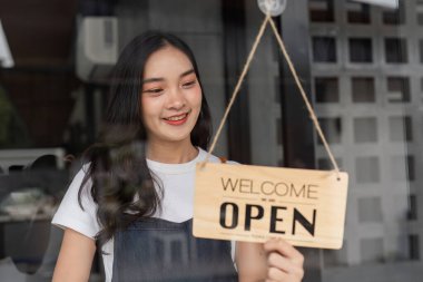 Barista bir kafe kapısına açık bir tabela astı, müşterileri karşılamaya hazırdı. Modern bir kahve dükkanında parlak ve davetkar bir atmosfer..