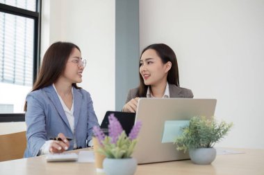 İki kadın muhasebeci, modern bir ofiste finansal grafikler ve veri analizleri üzerinde birlikte çalışarak takım çalışması ve profesyonel işbirliği sergilemektedirler..