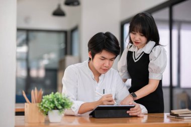 Üniversite öğrencileri ödev üzerinde birlikte çalışıyorlar, modern bir çalışma alanında dijital tablet kullanıyorlar. Ortak öğrenme ve takım çalışması.