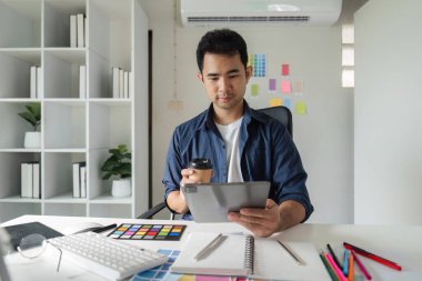 Modern ofis ortamında genç bir erkek grafik tasarımcısı bilgisayarında yoğun bir tasarım projesi üzerinde çalışıyor..
