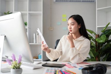 Grafik tasarımı alanında çalışan kadın tasarımcı grafik tasarımı için renk seçin. Bilgisayar üzerinde çalışmak için renkli kağıtlarla dolu bir masaya odaklanmış çalışma.