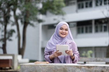 Confident Muslim girl student in hijab holding a notebook outdoors at a university campus, symbolizing education, learning, and academic success. clipart