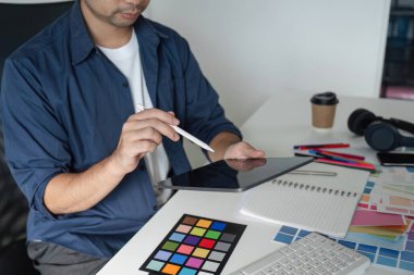 Tablet ve renk örnekleri kullanarak bir proje üzerinde çalışan grafiksel tasarımcı, modern ofis ortamında yaratıcılık ve planlama sergiliyor.