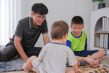 Bir baba ve iki oğlu birlikte boş zamanlarının tadını çıkarıyorlar, yerde oturup rahat bir ev ortamında eğlenceli aktiviteler yapıyorlar..