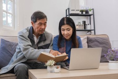 Yaşlı çift modern oturma odalarında dinleniyor, kitap okuyor ve dizüstü bilgisayar kullanıyor, rahat ve huzurlu bir ev ortamı sergiliyor..