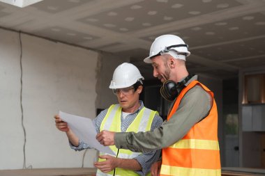 Mühendislik ekibi modern bir şantiyede inşaat planlarını planlar ve güvenlik teçhizatlarıyla tartışıyor..