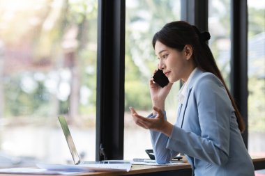 Zeki, modern bir ofiste çalışan genç muhasebeci, dizüstü bilgisayar ve akıllı telefon kullanıyor, finansal görevlere odaklanıyor, profesyonellik ve üretkenlik sergiliyor.