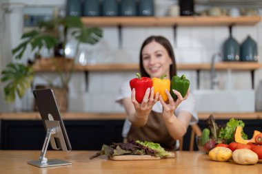 Modern bir mutfakta genç bir kadın taze sebzeli sağlıklı bir salata hazırlıyor, gülümsüyor ve elinde renkli dolmalık biber tutuyor..
