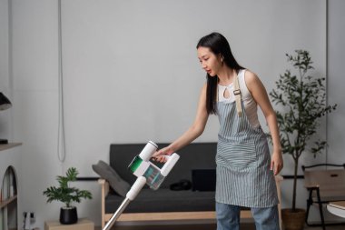 Genç bir kadın, minimalist ve düzenli bir ev ortamı sergileyerek modern bir oturma odasını temizliyor..