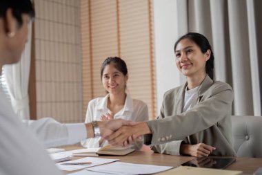 İş adamları modern bir ofiste el sıkışıyor, başarılı ortaklık ve işbirliğini simgeliyor..