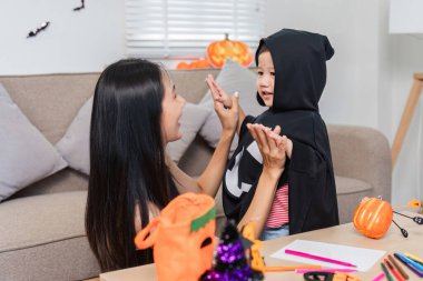 Bir anne ve kızı Cadılar Bayramı aktivitelerini yaparken neşeli bir anı paylaşıyor. Cadılar Bayramı süslemeleriyle çevrili, şenlikli kostümler giyiyorlar..