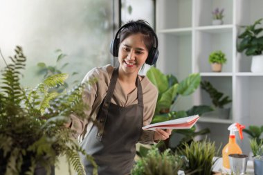 Genç bir kadın ev bitkileriyle çevrili küçük bir bahçe yetiştiriyor, modern bir odada yeşil yaşam ve rahatlığı teşvik ediyor..