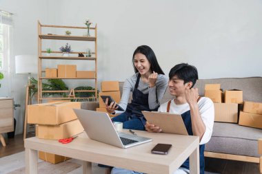 A young couple working together at home, taking online orders and packing products for their e-commerce business. clipart