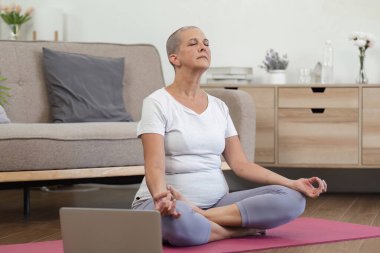 Evde yoga yapan yaşlı bir kadın sağlıklı ve aktif bir yaşam tarzı için kaslarını esnetmeye ve gevşetmeye odaklanıyor..
