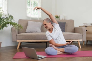 Yaşlı bir kadın evde yoga yapıyor ve kaslarını esnetiyor, sağlıklı ve aktif bir yaşam tarzını teşvik ediyor..