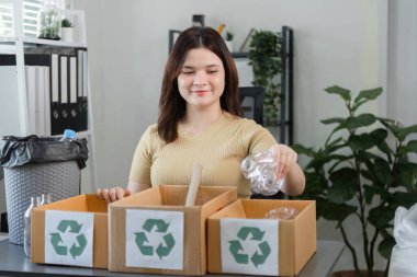 Bir kadın plastik atıkları geri dönüşüm kutularına ayırıyor, çevre dostu uygulamaları ve modern ortamlarda sürdürülebilirliği vurguluyor.