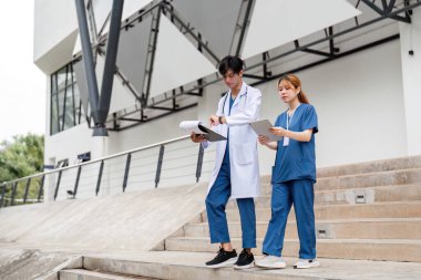 Hasta bakımı ve tıbbi kayıtları tartışan bir erkek doktor ve asistan, sağlık ortamında takım çalışması sergiliyor..