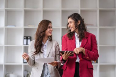 İki iş kadını, modern bir ofis ortamında takım çalışması ve profesyonel istişare sergileyen meslektaşlarıyla ortak bir tartışmaya giriştiler..